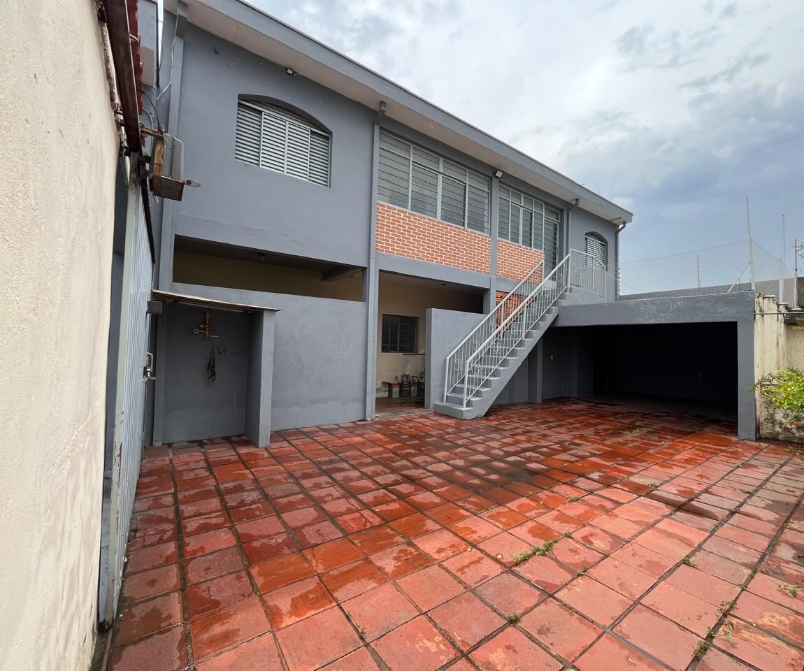 Quintal nos fundos com piso cerâmico vermelho, garagem coberta e escada externa que leva ao pavimento superior